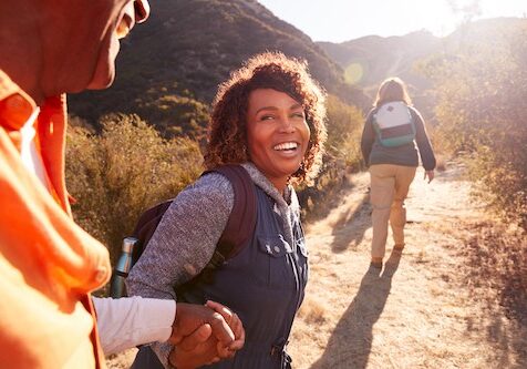 Woman Helping Man On Trail As Group Of Senior Friends Go Hiking In Countryside Together