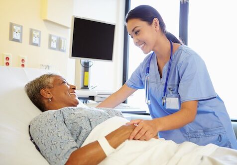 Happy Smiling Nurse Talking To Senior Woman In Hospital Room